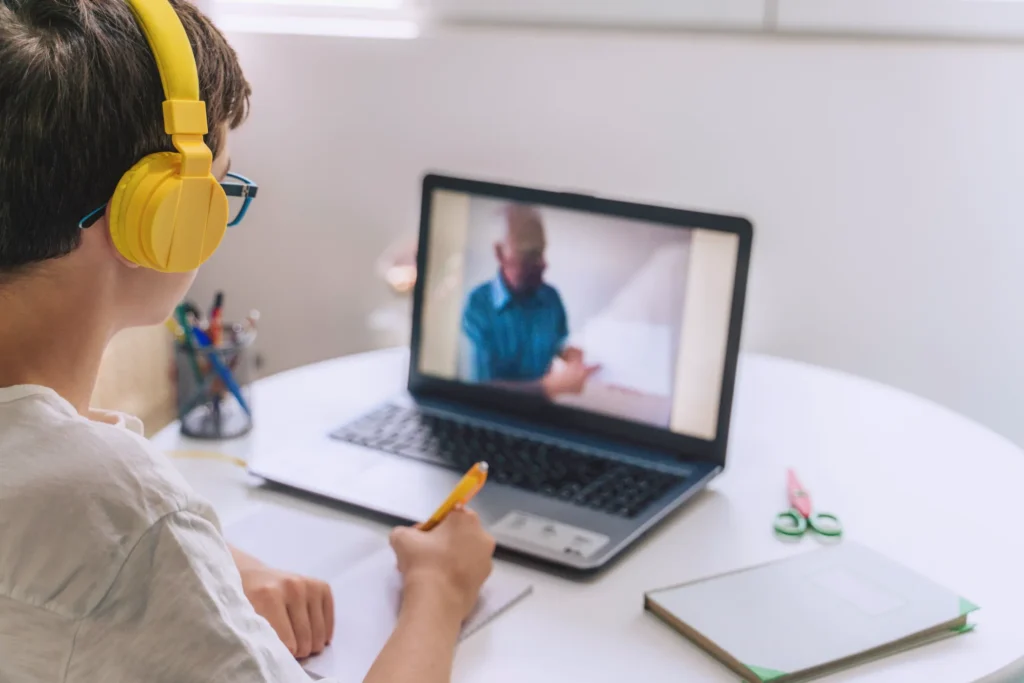 Uczeń słucha nauczyciela online i robi notatki przy biurku
